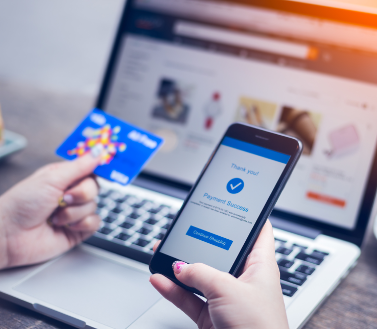 hands holding credit card and smartphone infront of open laptop